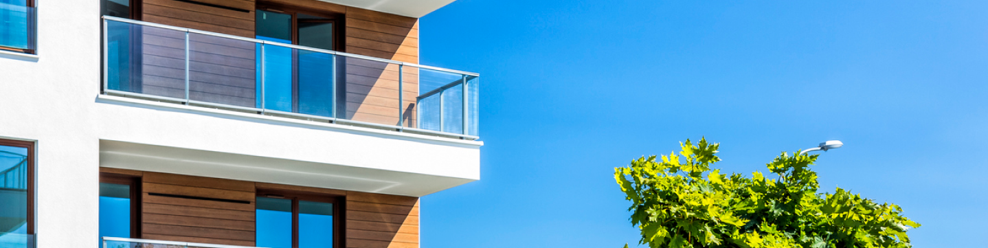 Un balcon d'un immeuble moderne, sur un ciel bleu, donnant sur un arbre.